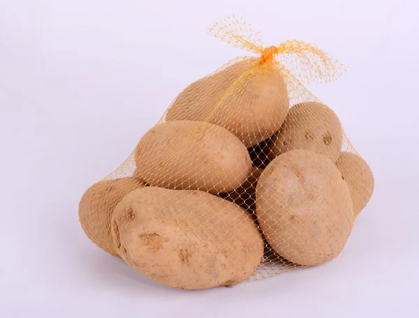 Heap of raw potatoes in yellow string bag. Isolated on white background. Close-up. — Stock Photo, Image