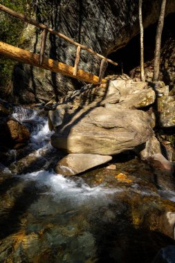 Küçük bir şelalenin üzerindeki kütük köprü Büyük bir kayalık boyunca