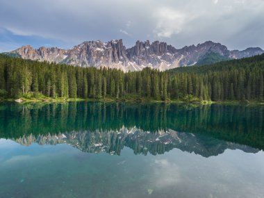 Latemar Sıradağları ve ormanda günbatımı bulutlu bir günde, Dolomites, İtalya, göl Carezza (Karersee) yansıyan