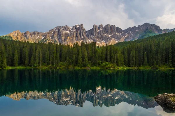 Latemar bergketen en bossen weerspiegeld in lake Carezza (Karersee) bij zonsondergang in een bewolkte dag, Dolomieten, Italië — Stockfoto