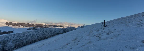 Fotografer berdiri sendiri di atas bukit dengan salju saat matahari terbenam, Sibil — Stok Foto