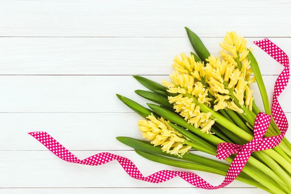 Bouquet de jacinthes jaunes orné de ruban rouge sur fond de bois blanc. Vue du dessus — Photo