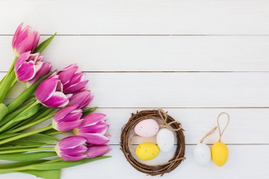 Pink tulips and decorative Easter eggs in small nest on white table. Top view