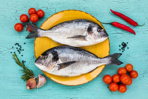 Peixe dorado cru fresco em prato amarelo e legumes em mesa azul. Vista superior — Fotografia de Stock