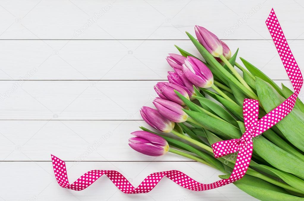 Bouquet of bright pink tulips decorated with pink ribbon on white wooden background. Top view