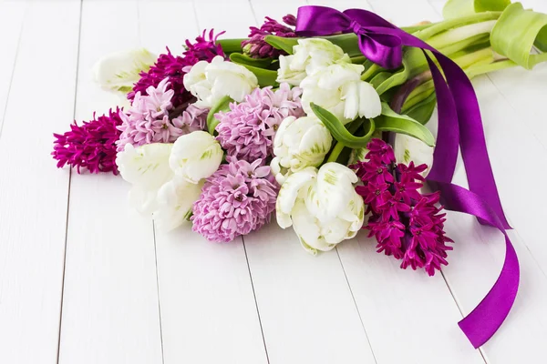 Букет весенних цветов украшен фиолетовой лентой на белом деревянном столе. Мягкий фокус — стоковое фото