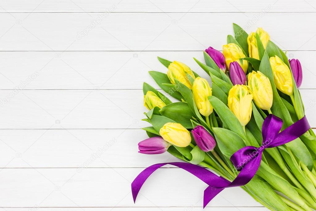 Bouquet of yellow and pink  tulips with purple ribbon on white wooden background. Top view
