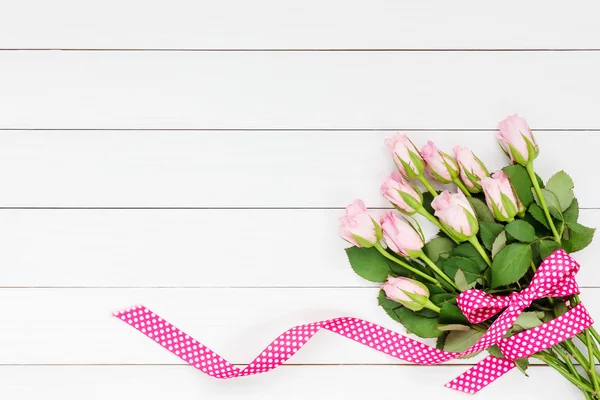 Bouquet of pink roses decorated with ribbon on white wooden background. Top view, copy space — Stock Photo, Image