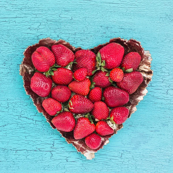 Mavi ahşap masa üzerinde kalp şeklinde plaka taze çilek. Üst te. Çilek kalp.