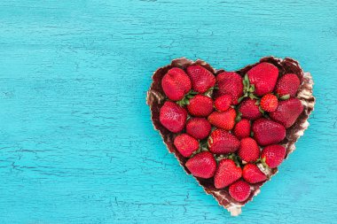 Mavi ahşap masa üzerinde kalp şeklinde plaka taze çilek. Üst te. Çilek kalp