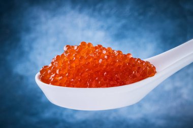 Mavi arka planda beyaz kaşıkta kırmızı havyar. Yemek arkaplanı. Metin için alanı kopyala