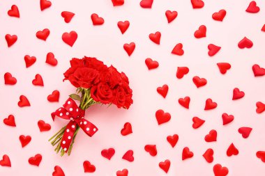 Sevgililer Günü konsepti. Kırmızı gül buketi ve pembe arka planda kırmızı kalpler. Üst görünüm
