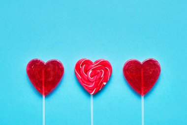 Sevgililer Günü konsepti. Mavi arka planda üç kalp şeklinde lolipop şekeri. Boşluğu kopyala, üst görünüm.