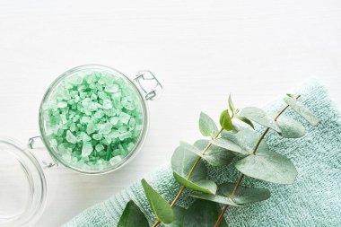 Havlu, banyo tuzu ve okaliptüs dalı beyaz ahşap arka planda. SPA konsepti