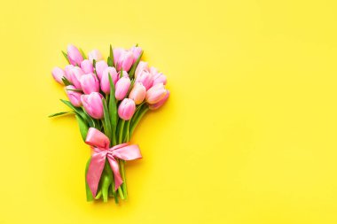 Parlak sarı arka planda kurdeleyle süslenmiş pembe laleler. Anneler Günü, Sevgililer Günü, doğum günü kutlaması konsepti. Üst görünüm, metin için boşluk kopyala