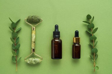 Yeşil yüzlü yeşil taştan bir silindir, koyu kahverengi cam damlalar tıbbi ve kozmetik kullanım için ve yeşil arka planda okaliptüs için. SPA konsepti. Üst görünüm, alanı kopyala