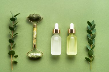 Yeşil yüz masajı silindiri, tıbbi ve kozmetik kullanım için cam damlaları ve yeşil arka planda okaliptüs. SPA konsepti. Üst görünüm, alanı kopyala