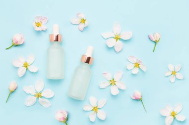Tıbbi ve kozmetik kullanım için hafif cam damlaları ve açık mavi arka planda elma ağacı çiçekleri. SPA konsepti. Üst görünüm, metin için boşluk kopyala