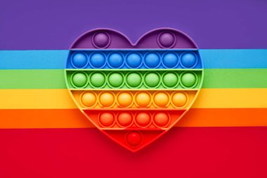 Renkli moda pop, oyuncağı gökkuşağı arka planında kıpır kıpır yapıyor. Oyuncak anti-stres, basit gamze. LGBT kavramı