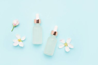 Kozmetik kullanım için iki cam damlası şişesi ve açık mavi arka planda elma ağacı çiçekleri. SPA konsepti