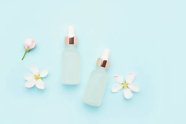 Dos cuentagotas de vidrio para uso cosmético y flores de flor de manzano sobre un fondo azul claro. Concepto SPA — Foto de Stock
