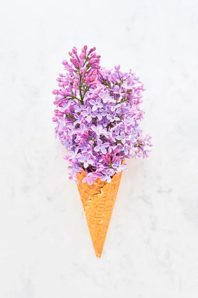 Cône de crème glacée gaufre avec fleurs rose lilas sur fond de marbre blanc. Concept de printemps — Photo