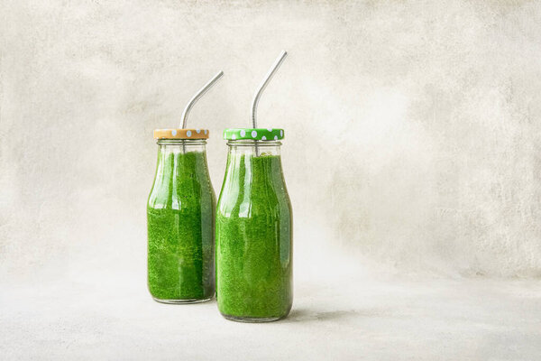 Green spinach smoothie in small bottles on a light background. Healthy lifestyle concept