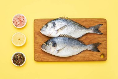 Baharatlı çiğ dorado balığı sarı arka planda tahta kesim tahtasının üzerinde.