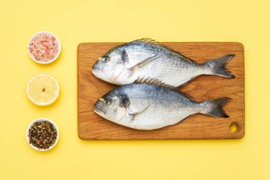 Raw dorado fish with spices on a wooden cutting board on a yellow background clipart