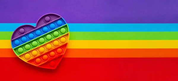 Banner. Colorido de moda Pop it corazón forma fidgets juguete para niños sobre un fondo de arco iris. — Foto de Stock