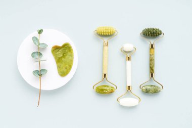 Guasha masaj aleti, yeşim yüz silindirleri ve gri arka planda okaliptüs dalları. SPA konsepti.