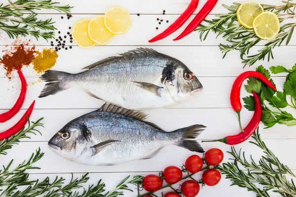 Ikan dorado segar, rosemary, lemon, tomat ceri, cabai di atas meja kayu putih. Tampilan atas — Stok Foto