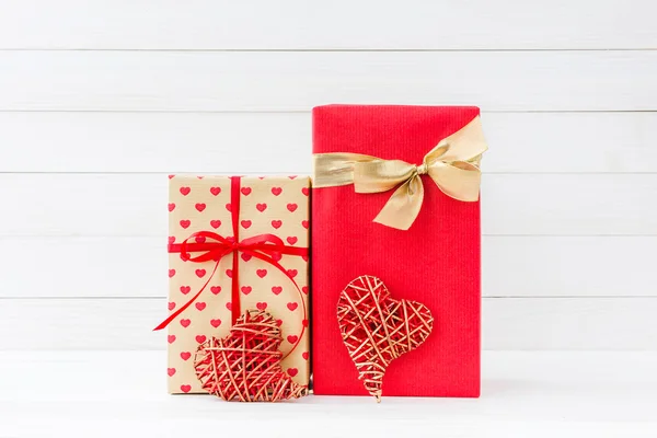 Sarılmış hediye kutuları ve Beyaz ahşap zemin üzerinde iki kırmızı kalp — Stok fotoğraf