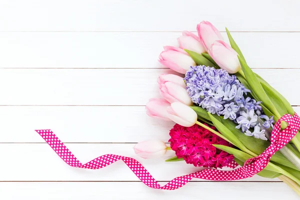Bouquet of spring flowers decorated with ribbon on white wooden background. — Stock Photo, Image