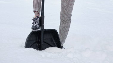Kürekle karları temizleyen kadın. Resimde, bir kadın bacağı, bir kürek ve kar.