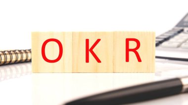 OKR symbol. Concept words OKR objectives and key results on cubes on a white background near a pen, calculator, notepad.