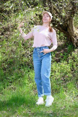 Bahar bahçesinde güzel bir kadın çiçek açan bir ağacın yanında duruyor, moda tarzı..