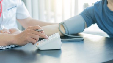 Arkadaki doktor basınç ölçer ile hastanın basıncını ölçer..