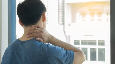 Mavi tişörtlü genç bir adam uzun çalışmanın ardından acıdan dolayı elini boynuna koydu. Yorgun ve endişeli hissediyordu..