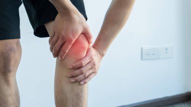 Beyaz bir arka planda kendi dizini acı içinde tutan genç bir adamın yakın çekimi. Kırmızı iltihap etkisi.