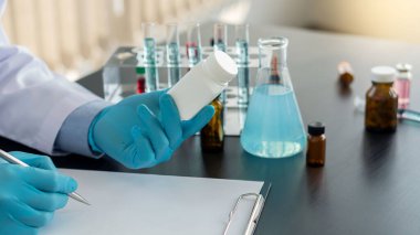 Doktorun elinde bir ilaç şişesi hastaya reçete yazan bir doktor. Ofiste oturan doktor. Aşı deney şişesi masanın üstünde.