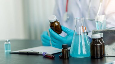 Doktorun elinde bir ilaç şişesi hastaya reçete yazan bir doktor. Ofiste oturan doktor. Aşı deney şişesi masanın üstünde.