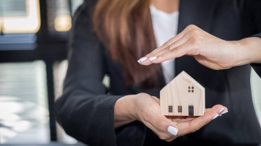 Genç bir emlakçı ya da banka memuru ofiste küçük beyaz bir ev tutuyor. Konut kredileri, Rüya Gayrimenkul Sigortası ve Gayrimenkul Konseptleri.