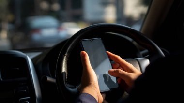 Simulated picture of the driver's hand using a smart phone, black screen inside the car, locating through a near-distance GPS navigation application, parked on the side of the road.
