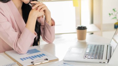 Young businesswoman analyzes cost graphs on desk in conference room with laptop