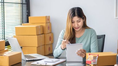 The right small business owner shoots a box of goods, ideas, startups and e-commerce. Asian business woman, online store manager, takes orders with laptop, packing box for delivery.
