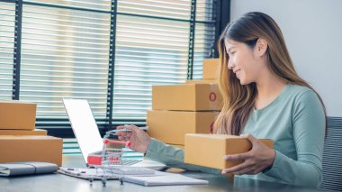 The right small business owner shoots a box of goods, ideas, startups and e-commerce. Asian business woman, online store manager, takes orders with laptop, packing box for delivery.