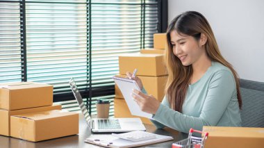 The right small business owner shoots a box of goods, ideas, startups and e-commerce. Asian business woman, online store manager, takes orders with laptop, packing box for delivery.