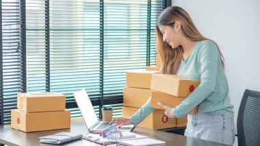 The right small business owner shoots a box of goods, ideas, startups and e-commerce. Asian business woman, online store manager, takes orders with laptop, packing box for delivery.