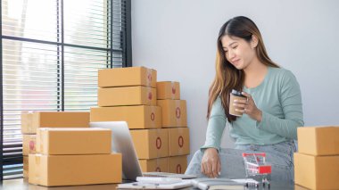 The right small business owner shoots a box of goods, ideas, startups and e-commerce. Asian business woman, online store manager, takes orders with laptop, packing box for delivery.